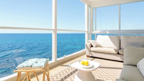 Een balkon met uitzicht op zee, een bank, een kleintje tafeltje met citroenen en een stoel met kussen.