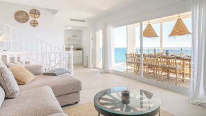 Un vaste espace de vie avec une grande fenêtre donnant sur la mer, un escalier blanc et un coin repas agrémenté de meubles en bois.