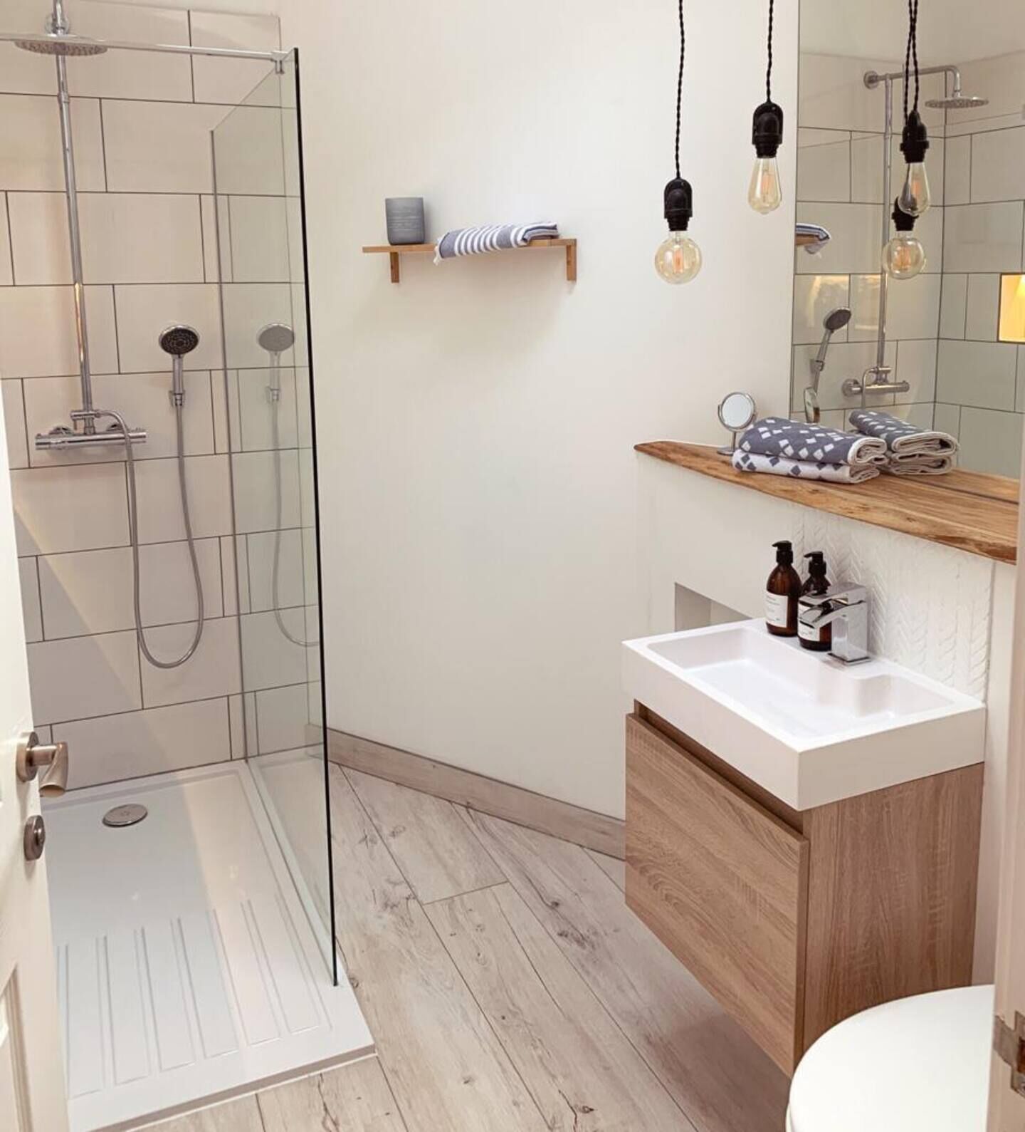 Ein modernes Badezimmer mit Duschkabine aus Glas, einem weißen Waschbecken mit Holdekor und einem Spiegel mit hängenden Glühbirnen.
