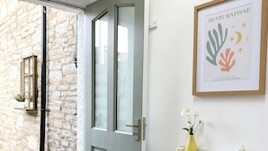 Une pièce moderne avec une chaise blanche, une porte donnant sur un mur en pierre, un radiateur et une œuvre d’art encadrée accrochée au mur.