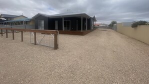 A residential property with a covered patio, a fenced yard, and a gravel driveway. - Lofty's Shack - Modern 3 bedroom, Free WiFi!, Off peak special! (Edithburgh)