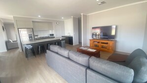 A modern living room with a grey sofa, a wooden coffee table, and a television on a wooden stand. - Lofty's Shack - Modern 3 bedroom, Free WiFi!, Off peak special! (Edithburgh)