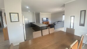A modern kitchen with a central island, a dining area with a wooden table and chairs, and a living area with a sofa and TV. - Lofty's Shack - Modern 3 bedroom, Free WiFi!, Off peak special! (Edithburgh)
