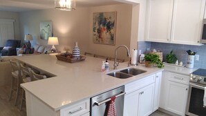 A modern kitchen with white cabinetry, a central island with a sink, and a dining area with chairs.