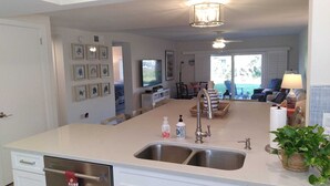 A modern kitchen with a central island, double sink, and a dining area with a TV.