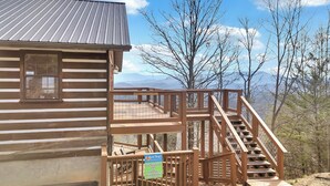 Una cabaña con terraza de madera y una escalera que lleva a un balcón.