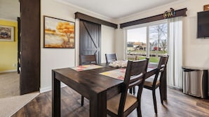 Un comedor con una mesa y sillas de madera oscura, un cuadro en la pared y vistas a través de amplios ventanales.