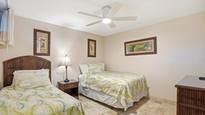A bedroom with two beds, a ceiling fan, and framed artwork on the walls. - Kamaole Nalu, #304 2 Bedroom Condo (Kihei)