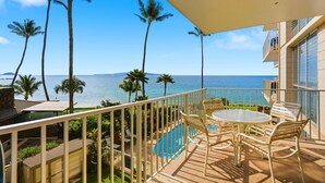 A balcony with a pool, chairs, and a view of the ocean and palm trees. - Kamaole Nalu, #304 2 Bedroom Condo (Kihei)