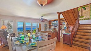 Un comedor con vista al océano, muebles de madera y una escalera que conduce a un nivel inferior.