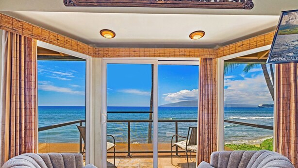 Habitación con un gran ventanal corredera que da a un balcón con vistas al océano. Hay dos sillas y una mesita en el balcón.