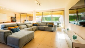 A modern living room with a sectional sofa, a flat-screen TV, and a large window offering a view of the outdoors.