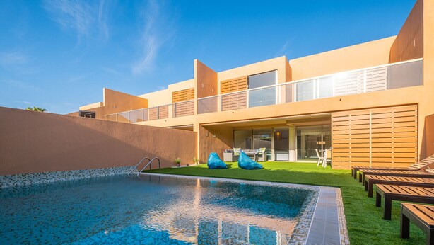 A modern building with a swimming pool, outdoor seating, and a well-maintained lawn.