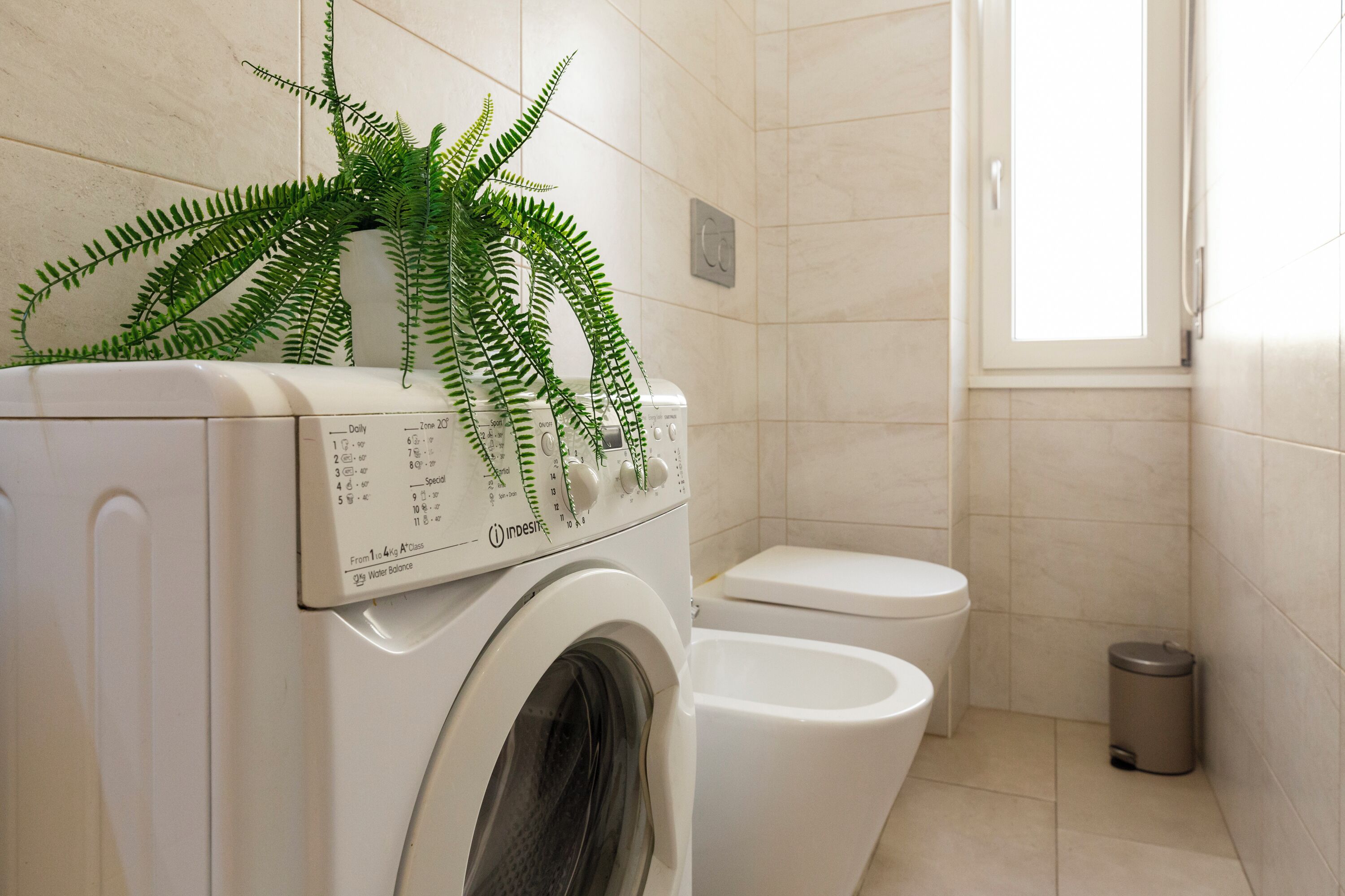 Une petite salle de bain équipée d’un lave-linge, de toilettes et d’une petite poubelle.