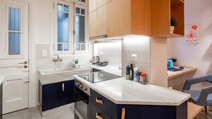 A modern kitchen with a built-in stove, sink, and a small dining area with a laptop and chair. - Historic 2BR Oasis in Kolonaki (Athina)