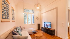 A modern living room with a sofa, a round wooden table, and a television on a black stand. - Historic 2BR Oasis in Kolonaki (Athina)
