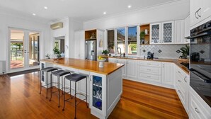A modern kitchen with white cabinetry, a wooden countertop, and a large island with bar stools. - Hubbard Hill Yarra Glen Oasis: 4-Bdrm Home with Pool & Stunning Valley Views (yarra glen)