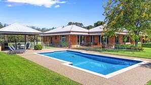 A swimming pool with a covered patio area, a brick house, and a lawn. - Hubbard Hill Yarra Glen Oasis: 4-Bdrm Home with Pool & Stunning Valley Views (yarra glen)