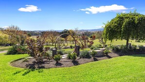 A landscaped garden with a circular metal sculpture, a large tree, and a grassy area. - Hubbard Hill Yarra Glen Oasis: 4-Bdrm Home with Pool & Stunning Valley Views (yarra glen)