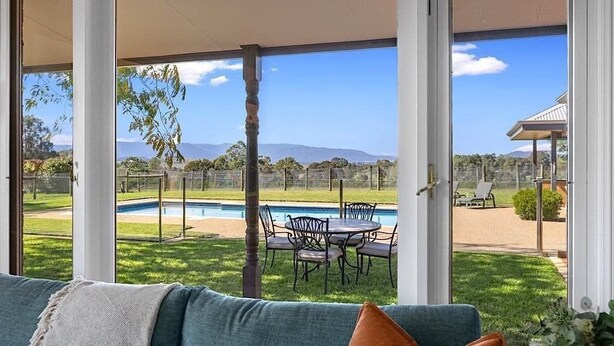 A room with a large window overlooking a pool and outdoor seating area. - Hubbard Hill Yarra Glen Oasis: 4-Bdrm Home with Pool & Stunning Valley Views (yarra glen)