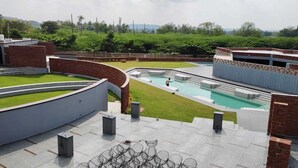 A rooftop pool area with a curved brick wall, a swimming pool, and a grassy lawn.