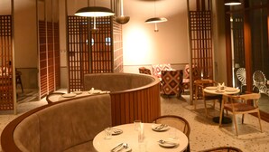A restaurant with a round table set for two, surrounded by cushioned seating.
