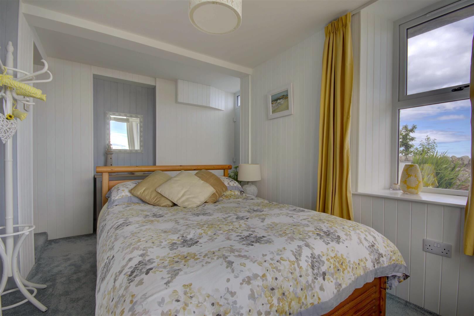 A bedroom with a bed, a window with curtains, a bedside lamp, and a view of the outdoors.