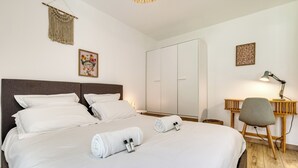 Una cama bien hecha con sábanas blancas, una toalla enrollada y dos botellas de artículos de tocador sobre la cama.