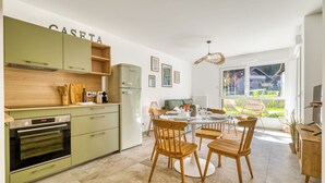 Una cocina compacta con horno empotrado, refrigerador y comedor con sillas y mesa de madera.