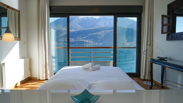 Een hotelkamer met een groot bed, uitzicht op zee en bergen, en een balkon met een hekwerk.