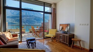 Een ruime woonkamer met een groot raam en uitzicht op bergen, een gezellige bank, een houten salontafel en een flatscreen televisie op een kast.