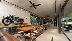 A modern dining area with a long wooden table, cushioned chairs, and a ceiling fan. - Palm Villa (Mang Yang)