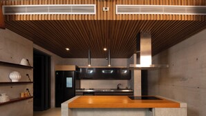 A modern kitchen with a central island, built-in appliances, and wooden ceiling panels. - Palm Villa (Mang Yang)