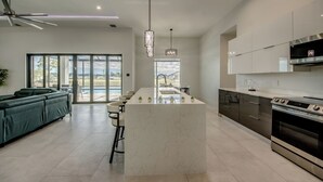 Une cuisine moderne dotée d’un îlot central, d’appareils électroménagers en acier inoxydable et d’une grande fenêtre offrant une vue sur l’extérieur.