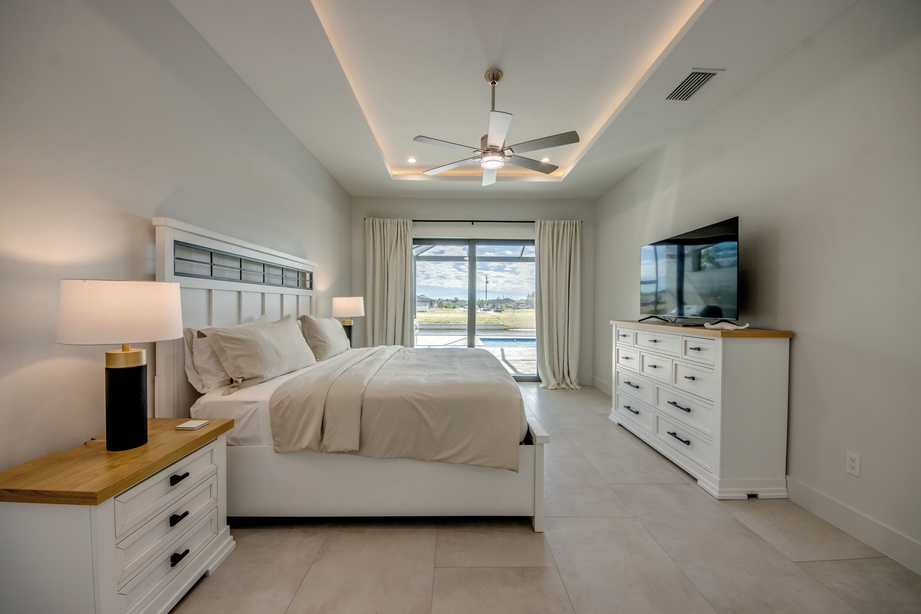 A modern bedroom with a bed, bedside table, TV, and a view of the outdoors.