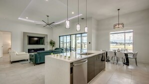 Une cuisine moderne avec un îlot central, un coin repas avec des chaises, un canapé et un téléviseur fixé au mur.