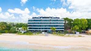 A modern multi-story hotel with a beach view, located on a sandy shore. - Luxurious Oceanfront Condo with Rooftop Pool on Brighton Beach– Sleeps 4 (Bridgetown)