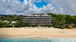 A multi-story hotel with balconies, located on a beach with clear turquoise waters and sandy shores. - Luxurious Oceanfront Condo with Rooftop Pool on Brighton Beach– Sleeps 4 (Bridgetown)