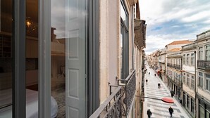 A narrow street with buildings on either side, a pedestrian walkway, and a view of a hotel room with a bed and a hanging light fixture. - Cosy studio - Old Porto (Porto)