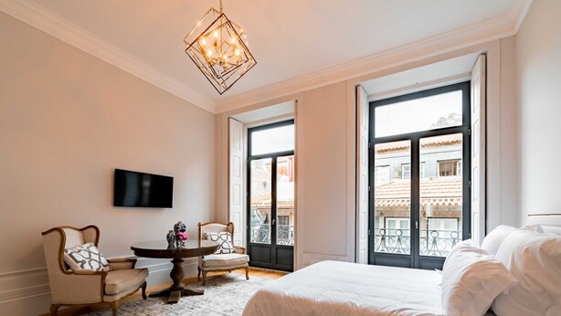 A bedroom with a large bed, a television mounted on the wall, a dining table with chairs, and a view of the outside through large windows. - Cosy studio - Old Porto (Porto)