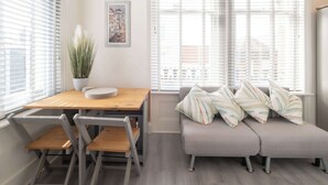 A modern living space with a wooden dining table, a gray sofa with patterned cushions, and a potted plant. - Host & Stay | Harbour Point (Ramsgate)