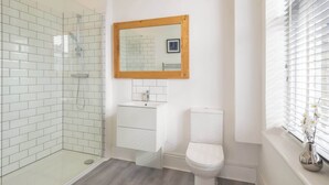 A modern bathroom with a glass shower enclosure, a white toilet, and a wooden-framed mirror above the sink. - Host & Stay | Harbour Point (Ramsgate)