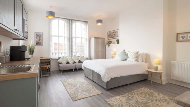 A modern bedroom with a large bed, bedside tables, a sofa, and a kitchen area with a coffee machine. - Host & Stay | Harbour Point (Ramsgate)
