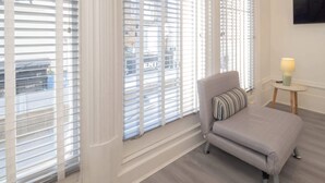 A bedroom with a bed, a chair, a small table with a lamp, and large windows with blinds. - Host & Stay | Harbour Rest (Ramsgate)
