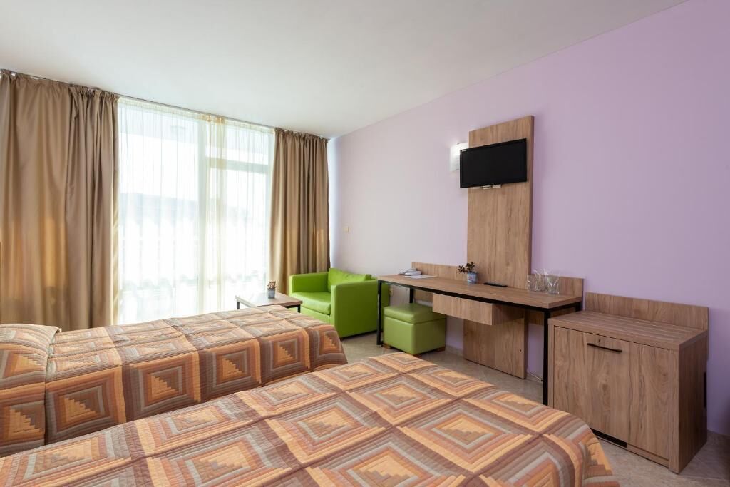 Ein Hotelzimmer mit einem großen Bett, einem Schreibtisch, einem Sessel und einem an der Wand befestigten Fernseher.