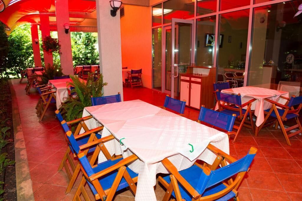 Un restaurant en plein air avec des tables et des chaises, un sol carrelé de tuiles rouges et des portes vitrées donnant sur l’intérieur.