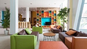 A modern interior with green and brown sofas, a TV, and colorful shelving units. - Hotel Ivana Palace (Sunny Beach)
