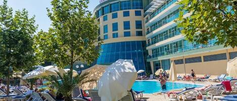 A hotel with a pool area, lounge chairs, and umbrellas.