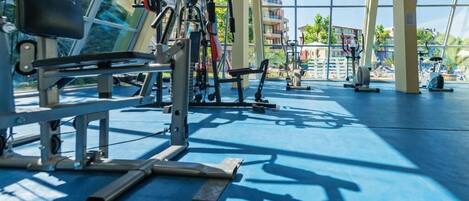 A gym with various exercise equipment, large windows, and a blue floor.