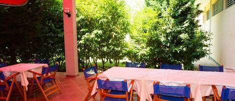 Eine Terrasse im Freien mit Tischen und Stühlen, umgeben von Bäumen.
